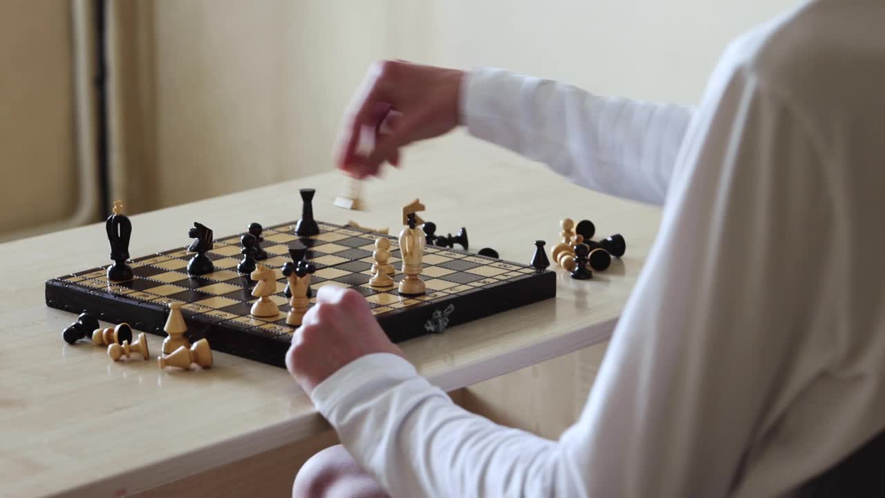 一个人坐在桌旁下棋。他们移动棋盘上的一个棋子视频素材