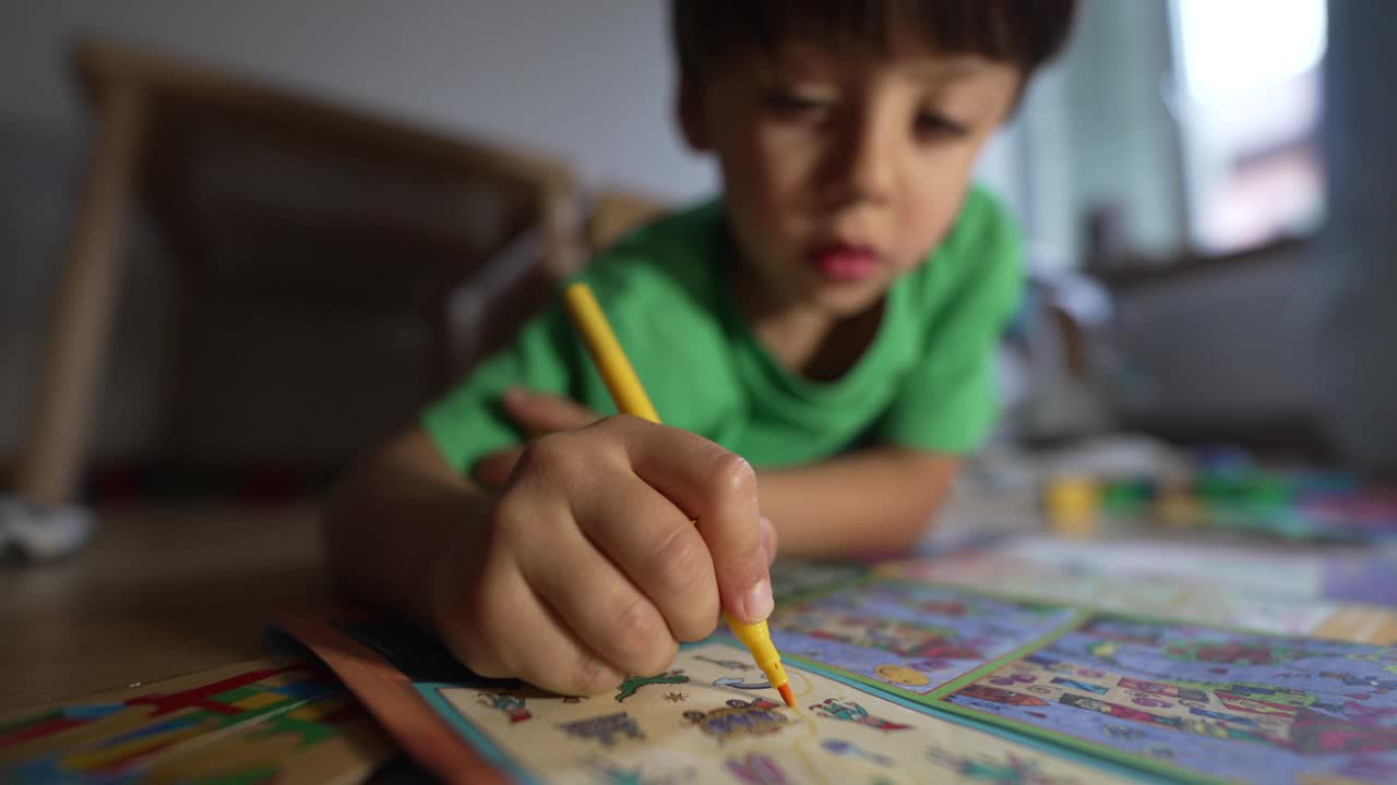 幼儿专注于填色书，用黄色记号笔画画，躺在家里的地板上，绿色衬衫，创造性活动，室内，自然光，童年的乐趣视频素材