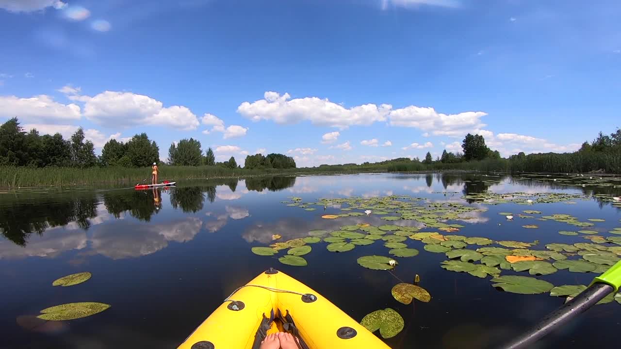 在一个阳光明媚的夏日里沿着河划皮艇。在风平浪静的日子里，一个人在河上的船上漂浮，水面上反射着白云。旅游业。积极的生活方式。活动。观点视频素材