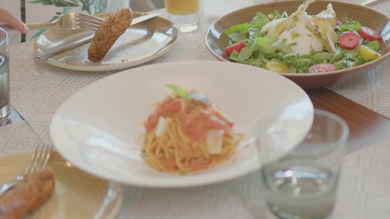 在昂贵的豪华饭店的餐厅里，一家人坐在餐桌旁。沙拉、意大利面、装有果汁和鸡尾酒的酒杯都在桌子上视频素材