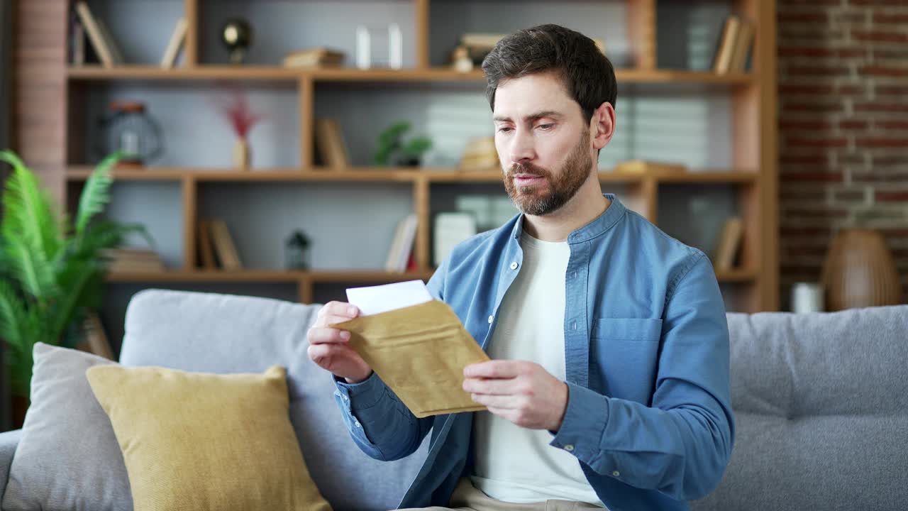 失望的帅哥坐在家里的沙发上读着带坏消息的信视频素材