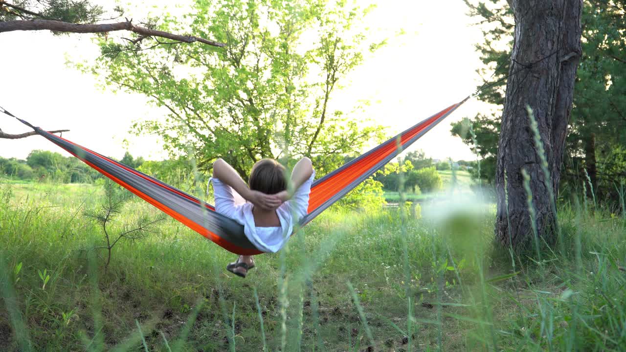 夏天，一位妇女在户外的吊床上休息。视频下载