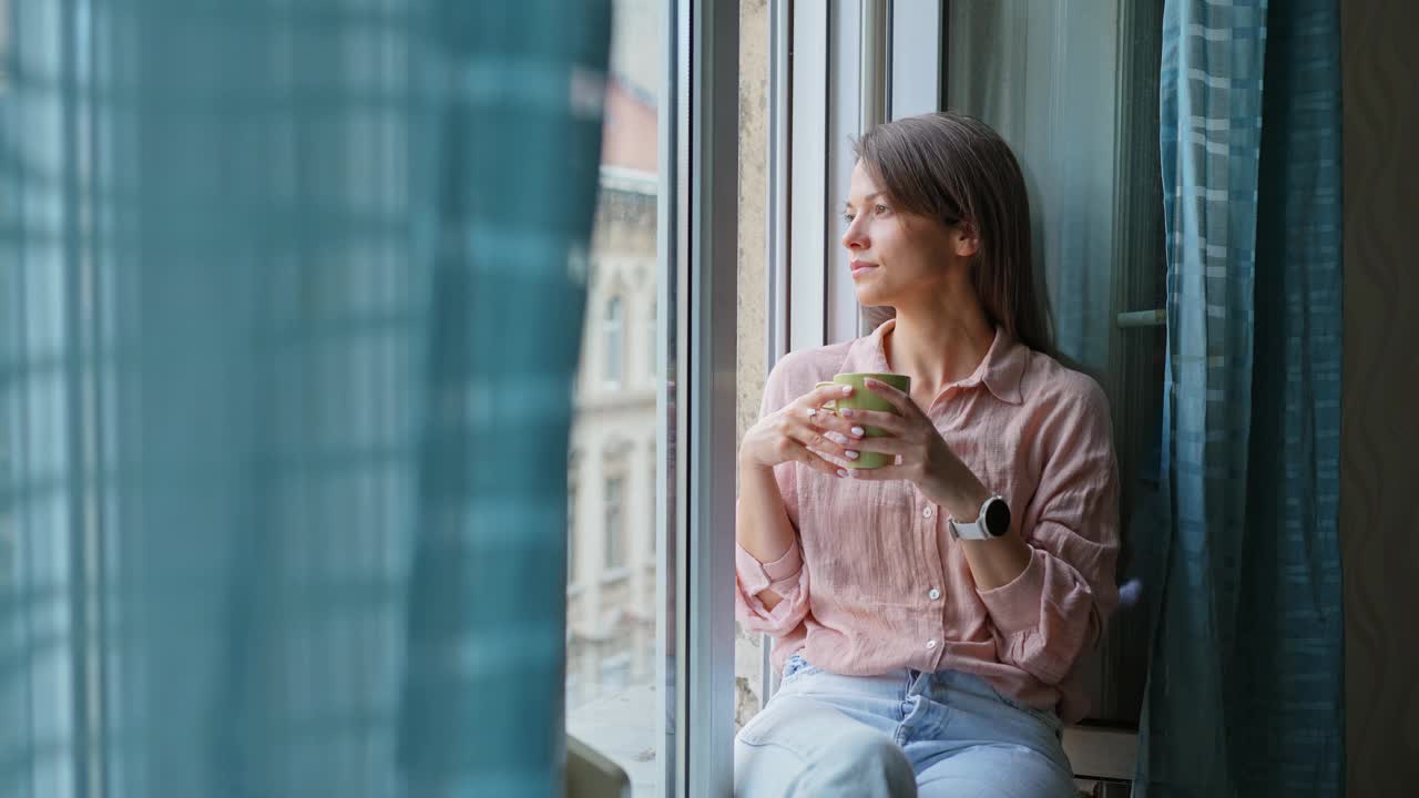 年轻女子边看窗外边喝咖啡视频素材