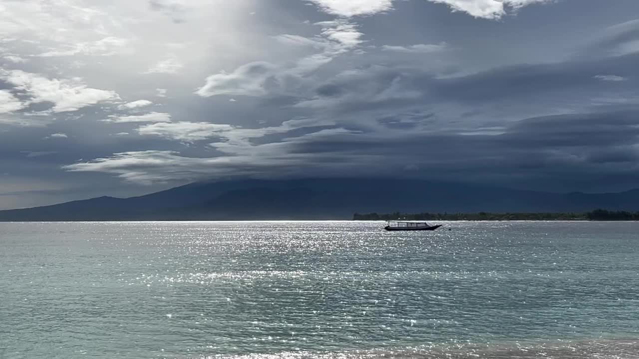 孤独的船在波光粼粼的海洋在阴天和阳光明媚的日子附近的吉利梅诺海岸线，印度洋，巴厘岛，印度尼西亚视频下载