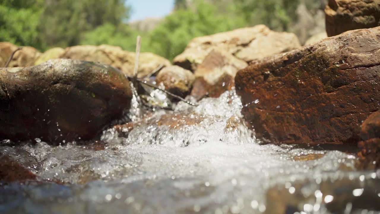 一股水流在大岩石之间流动，镜头向上移动，一个小湖泊出现。这是一片宁静祥和的景象视频下载