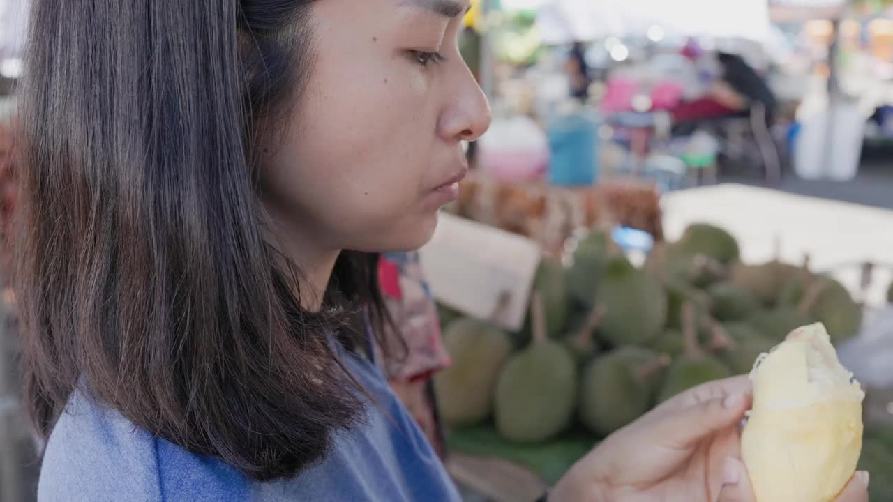 亚洲妇女在泰国水果市场吃新鲜的榴莲皮。视频下载