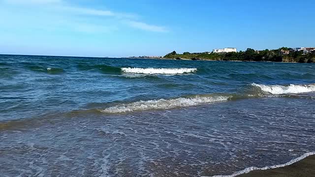 阳光明媚的夏日，风景如画的海景。小波浪拍打着海岸，山脉和度假小镇在地平线上清晰可见。在保加利亚黑海海岸度假，Kiten镇，南海滩视频下载