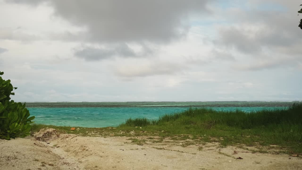 一个穿着浅色衣服、戴着帽子的年轻人向海边走来。背景是大海和暴风雨的黄昏云。视频素材