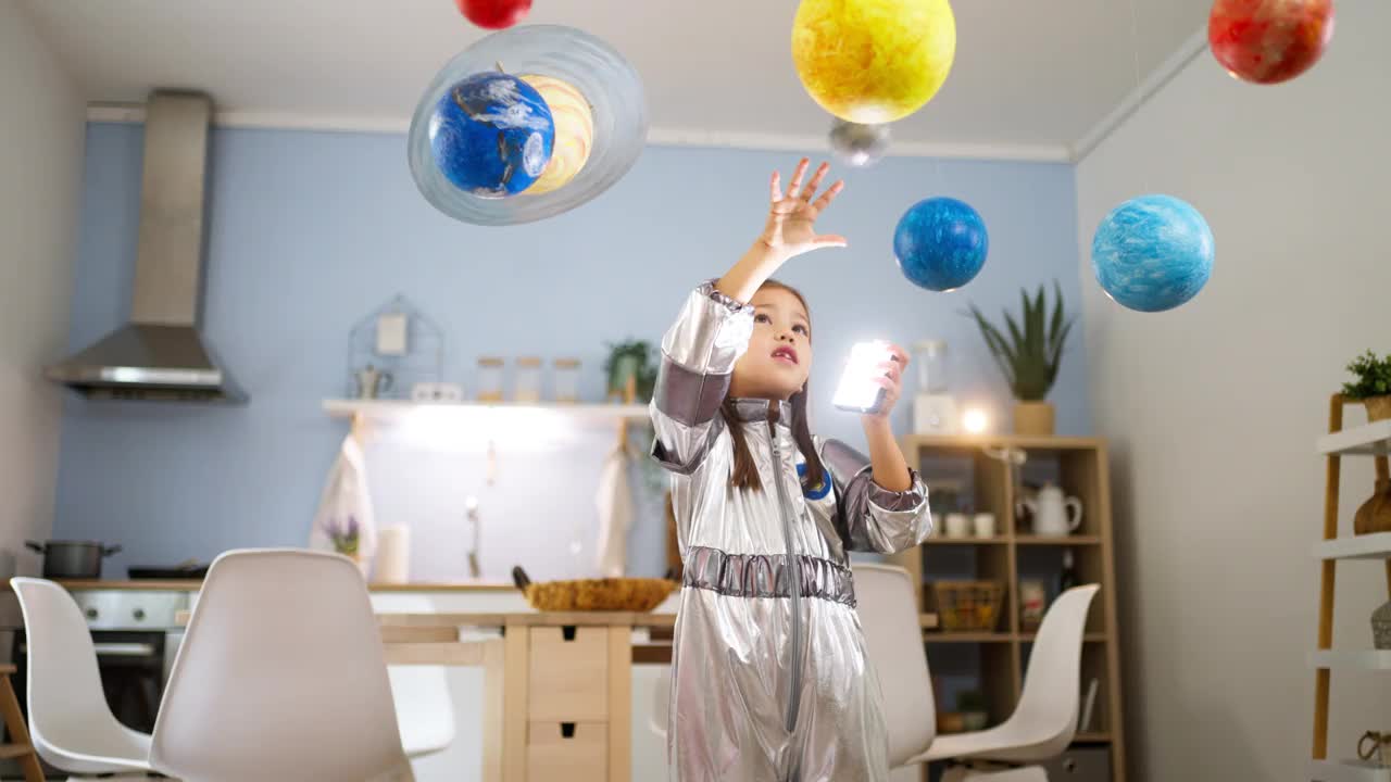 穿着太空服的女孩在家里玩耍，探索和学习行星，想象太空旅行。视频素材