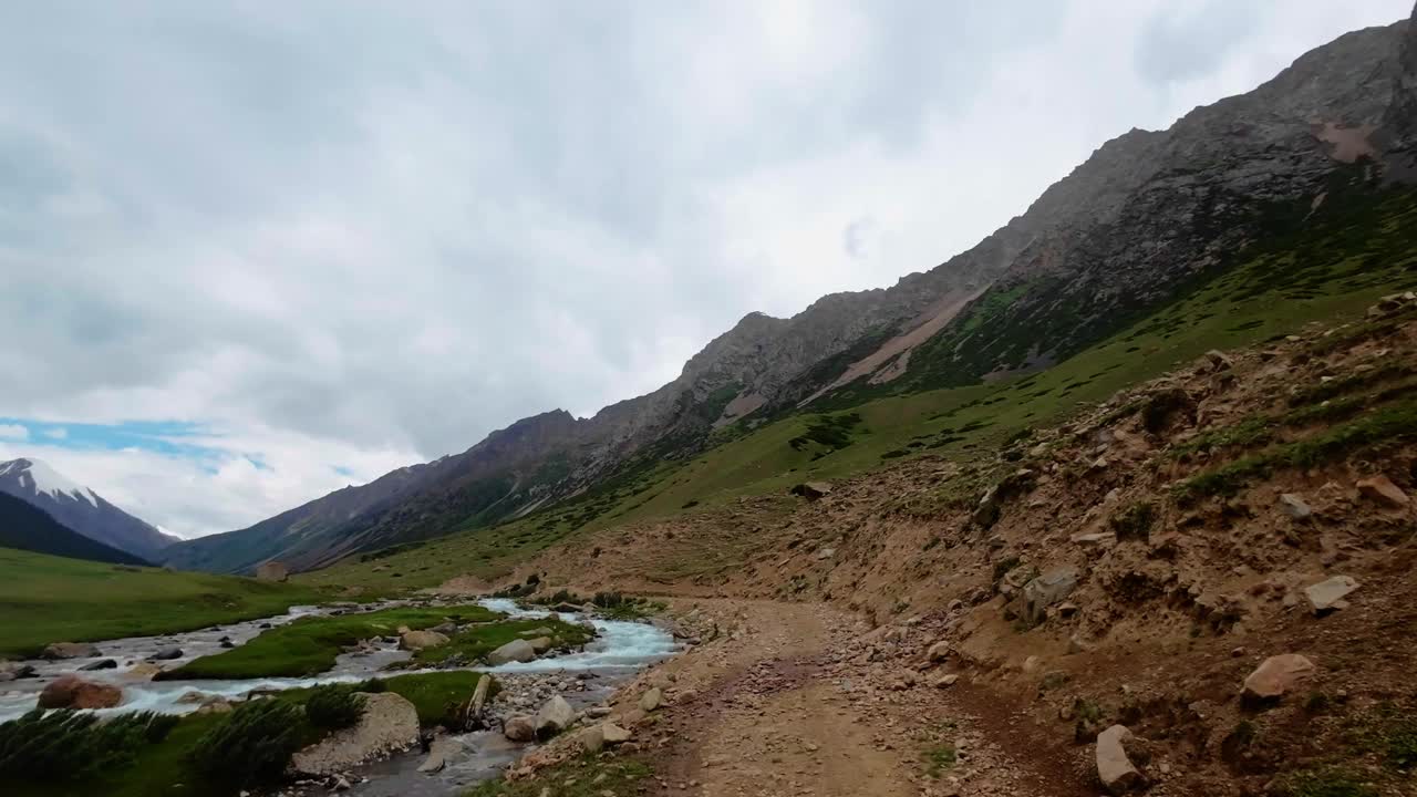 在多云的天空下，沿着夏季峡谷的山河岸上的岩石小径航行视频素材