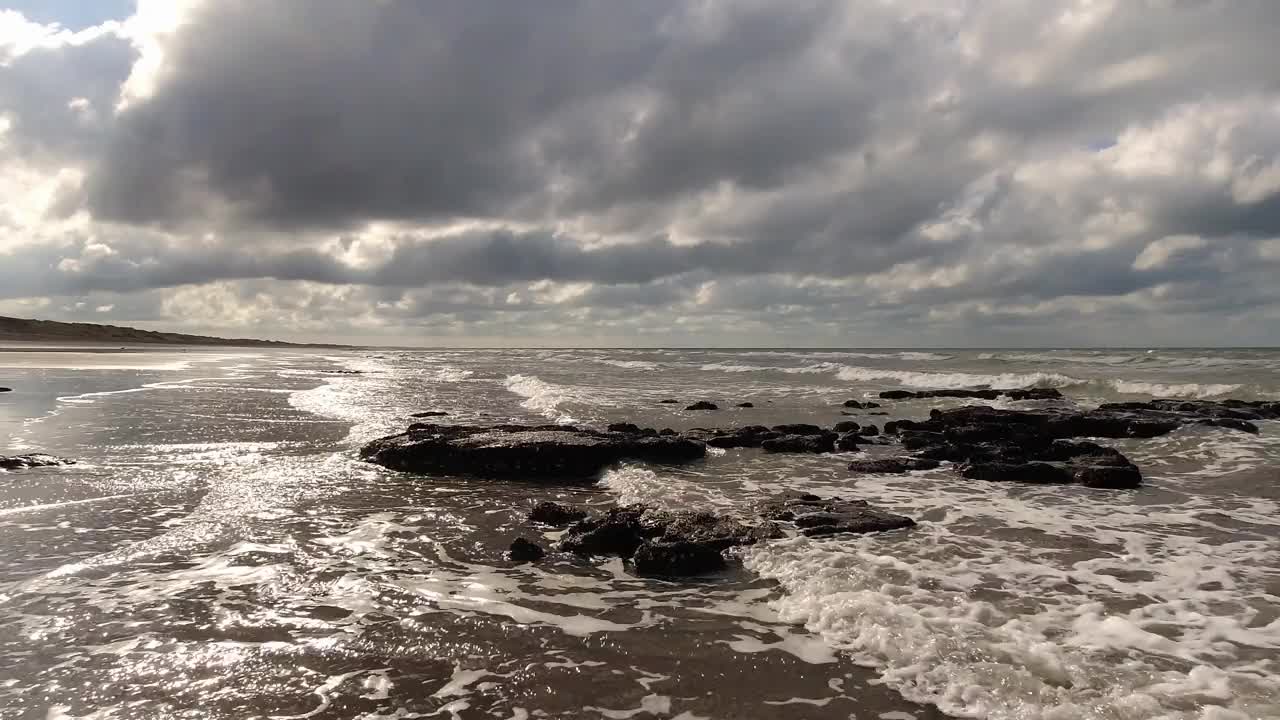 宁静的海浪流过岩石和沙子在海滩海岸。4 k的片段视频下载