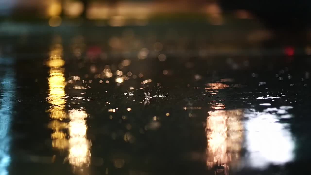 夜城暴雨的大气视频。大雨和汽车从低洼处经过的水坑溅起的水花。在街灯的照耀下，大雨滴落在人行道上视频下载