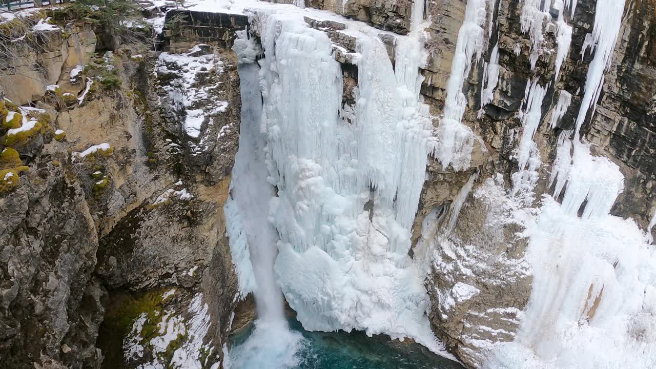 鸟瞰冰冻瀑布与冰冷的岩石和流动的水。冰天雪地的冬日景观。神奇的大自然冬天。纯净的冰川水。加拿大班夫著名的旅游景点。视频下载