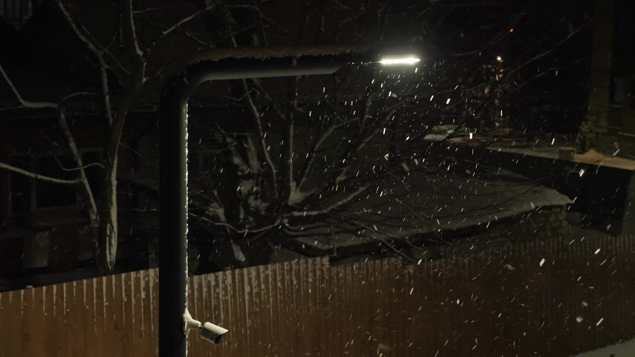 街道上的雪夜灯火通明。雪花在黑暗中飘落视频下载