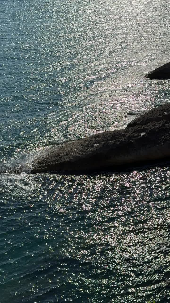 大海深蓝色的海水闪闪发光，与海岸的岩石，垂直视频。视频素材