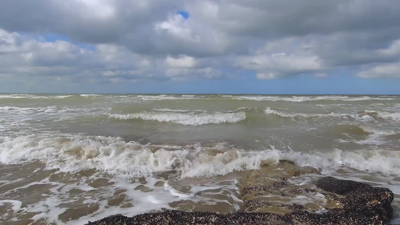 海浪拍打着海滩海岸线上布满软体动物的岩石。蓝天白云，4k 60 fps视频下载