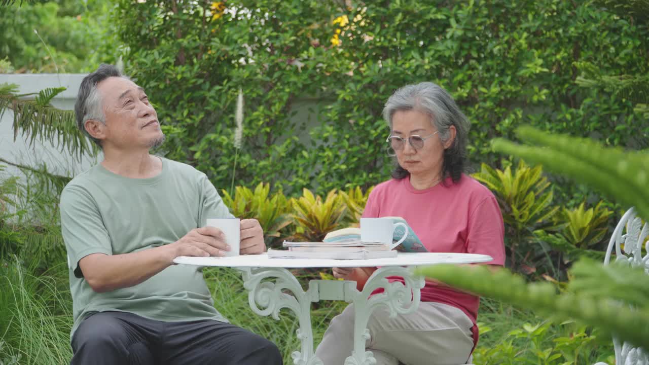 一对年老的亚洲夫妇一起看书，在温暖的春日夜晚在自家的花园里度过。视频下载