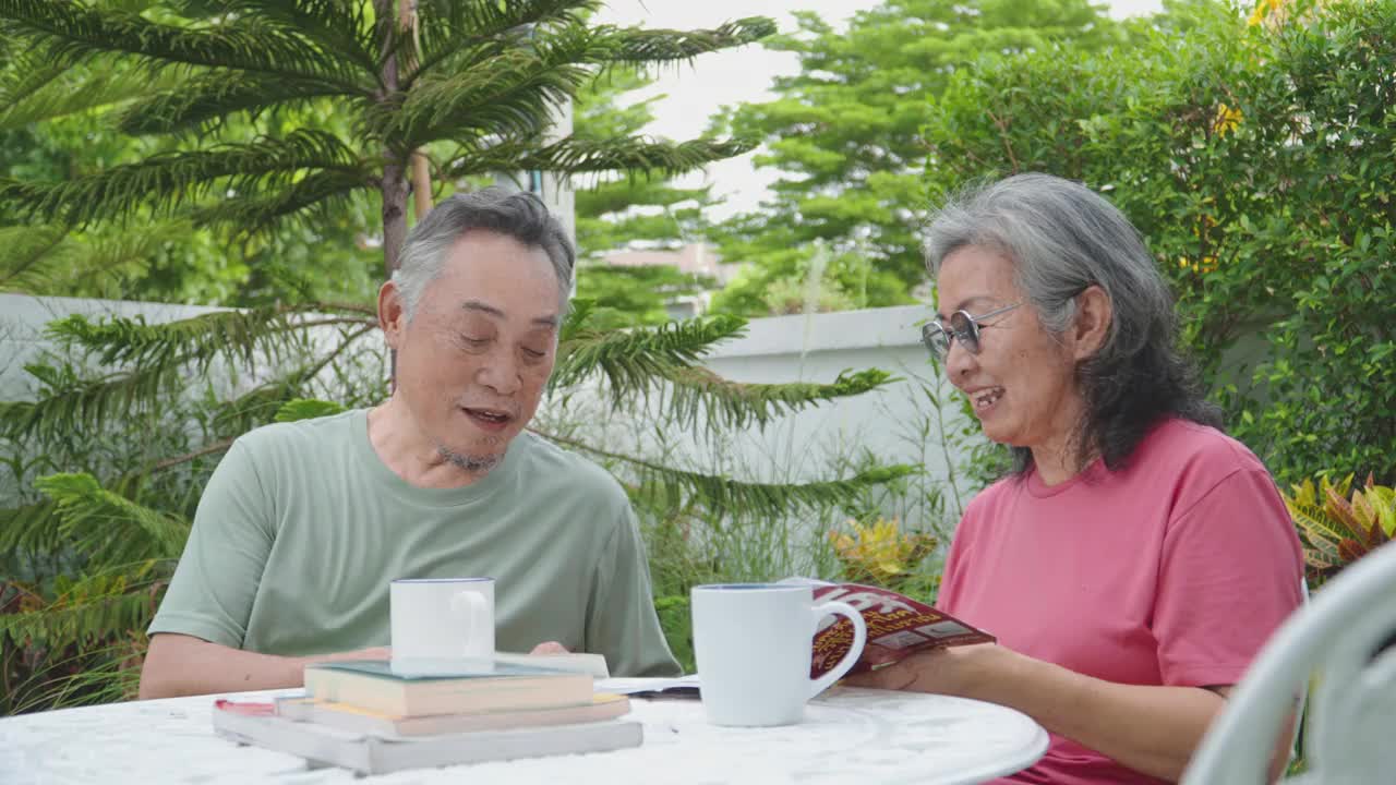 一对年老的亚洲夫妇一起看书，在温暖的春日夜晚在自家的花园里度过。视频下载