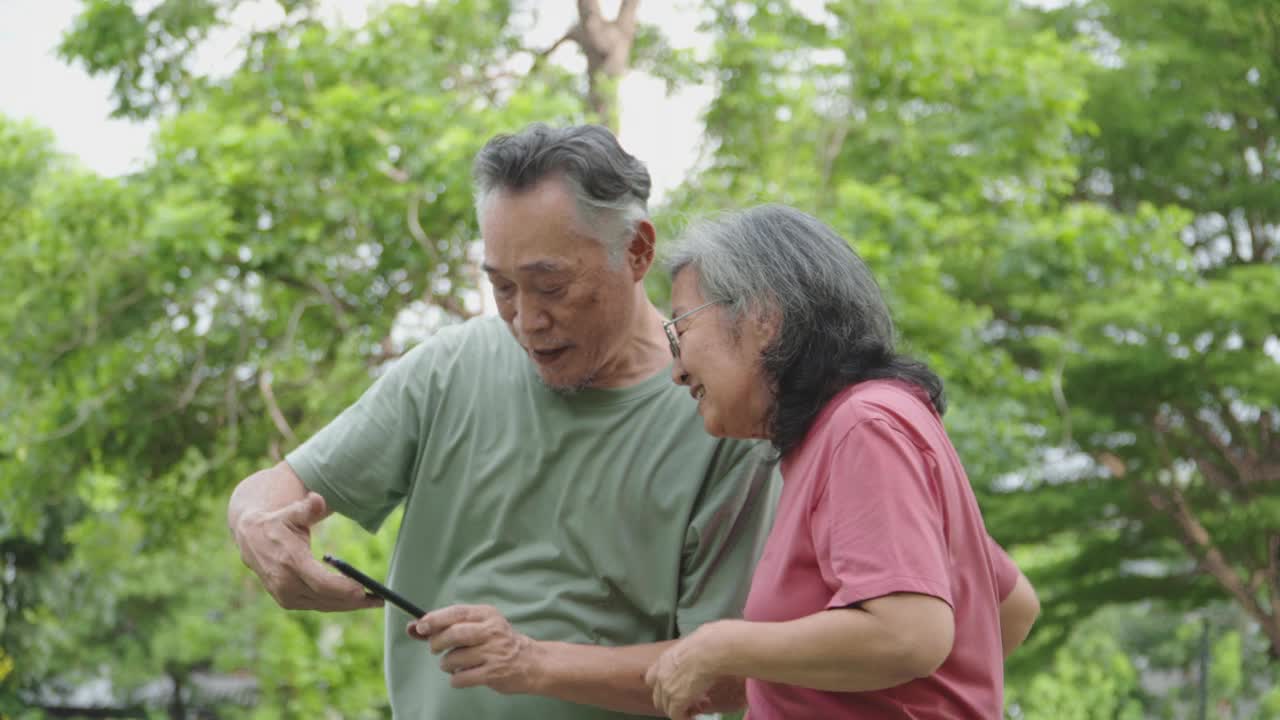 一名老年男子和一名亚洲女子在花园里用智能手机自拍。视频下载