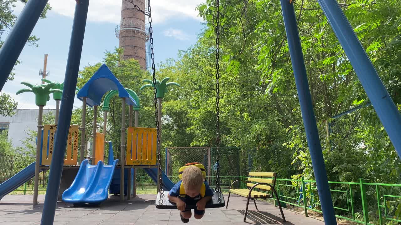 小孩子在夏天的操场上玩耍，小男孩在秋千上荡秋千视频素材