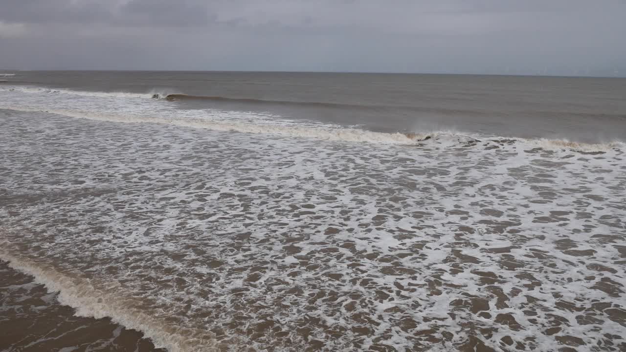 在英国海岸的一个灰色的日子里，来自北海的温柔的海浪翻滚到海岸的海滩上，有白色的海浪视频素材