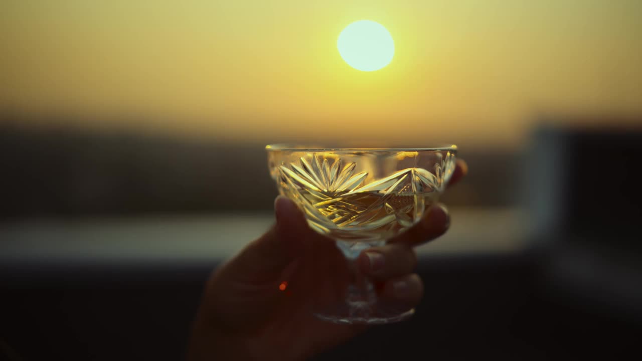 手拿着一瓶复古的香槟水晶杯，在夕阳的余晖中，阳光透过水晶杯洒下视频下载