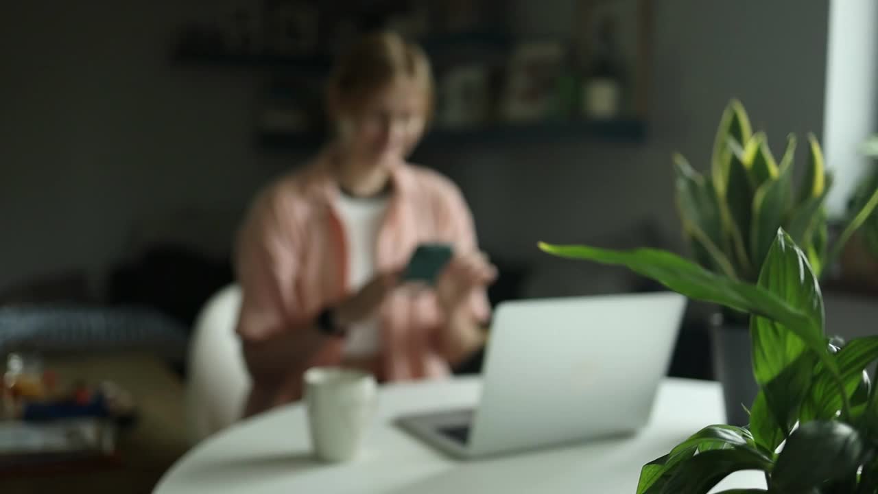 年轻的女学生在室内用手机和笔记本电脑准备作业。白人妇女在智能手机上搜索项目信息。自由家庭教育视频下载