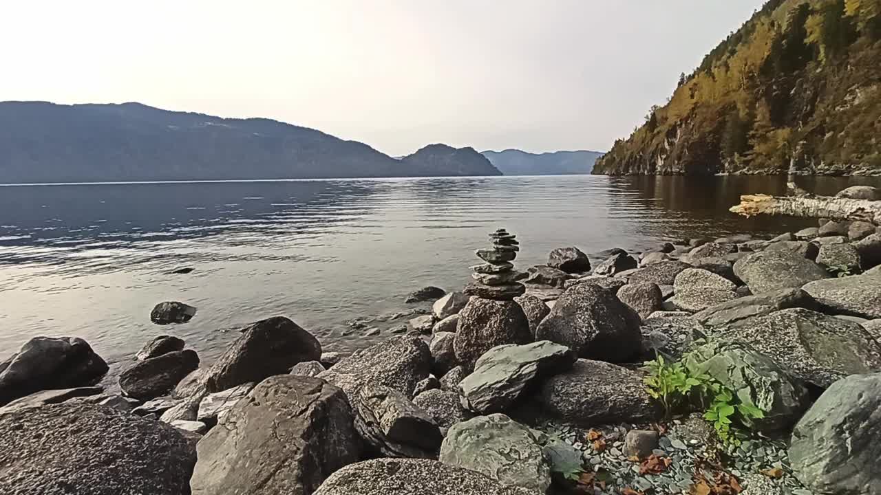 在一个多云的秋夜，在高山环绕的大湖岸边的神圣的石头金字塔。视频下载