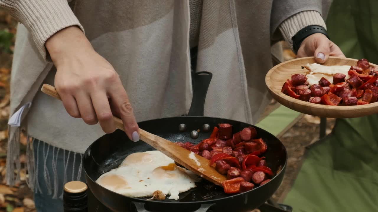 妇女在大自然中使用煎锅和便携式燃气加热器做饭。女性的手从煎锅里取出热的食物放在木盘上视频下载