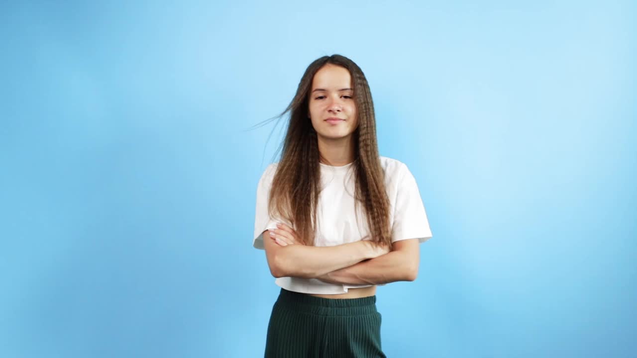 青少年肖像蓝色背景，年轻可爱自信的学生双臂交叉，开朗的脸与积极的表情，时尚的青年模型视频素材