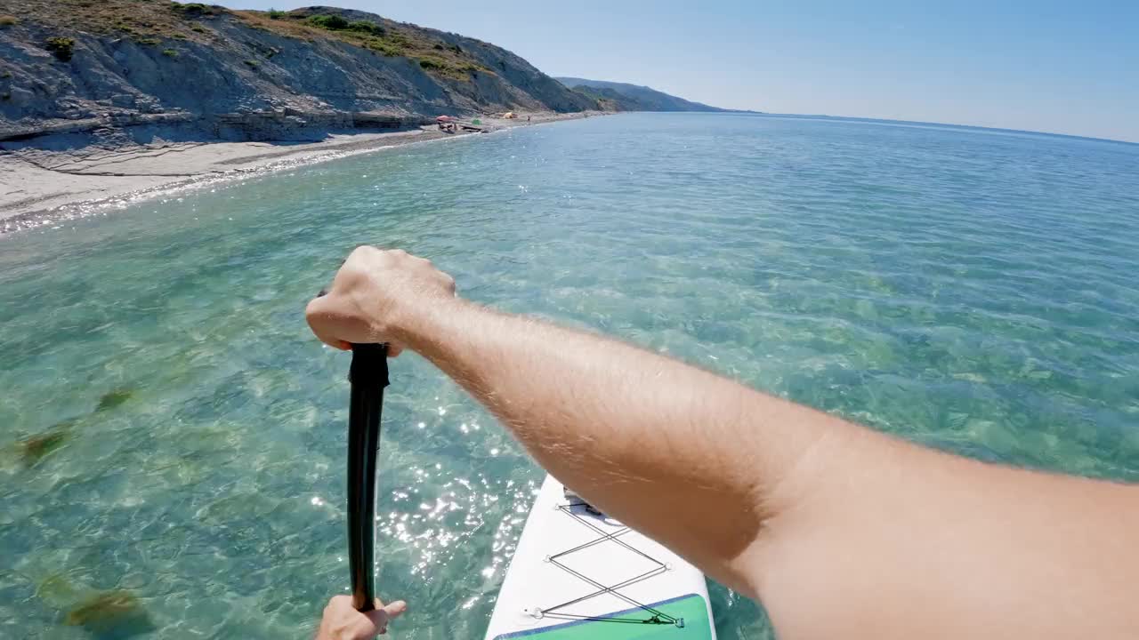 人们在透明的海面上划桨。夏季站立桨板的第一人称视角。视频素材