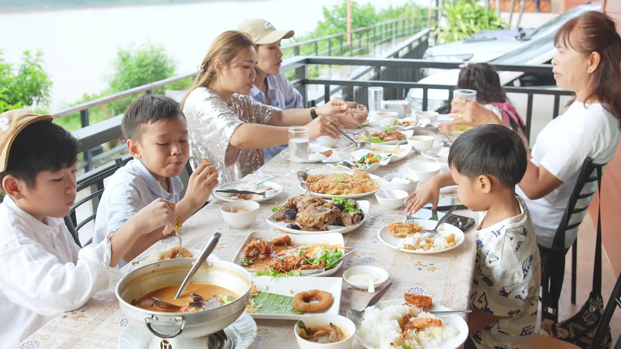 亚洲家庭成员愉快地共进晚餐，在餐桌上交谈和交换意见。这是一个快乐的时间在河边的餐馆。视频素材