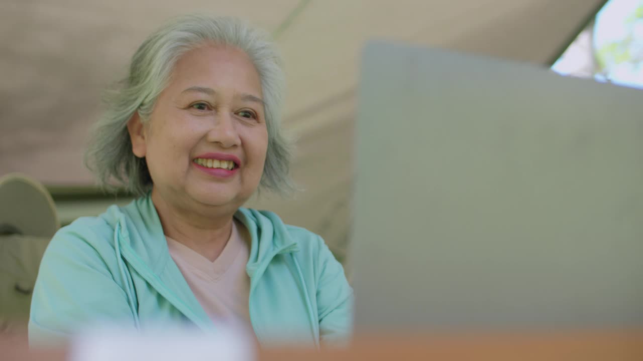 年长的女性旅行，坐在帐篷里，用笔记本电脑聊天，面带微笑视频素材