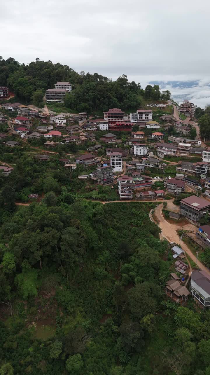 空中拍摄的照片显示，在一个阴天，一个山村的房子坐落在郁郁葱葱的绿色植物和蜿蜒的道路之间视频下载