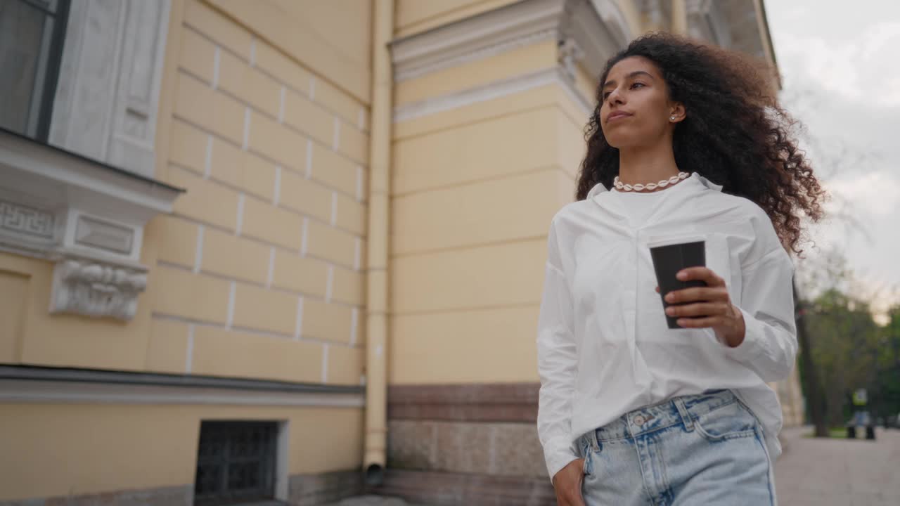 美丽的多民族女人，手里拿着咖啡杯走在城市的街道上。市中心女性路人的中等肖像，在欧洲城市旅行的漂亮阿拉伯女学生，慢动作视频素材