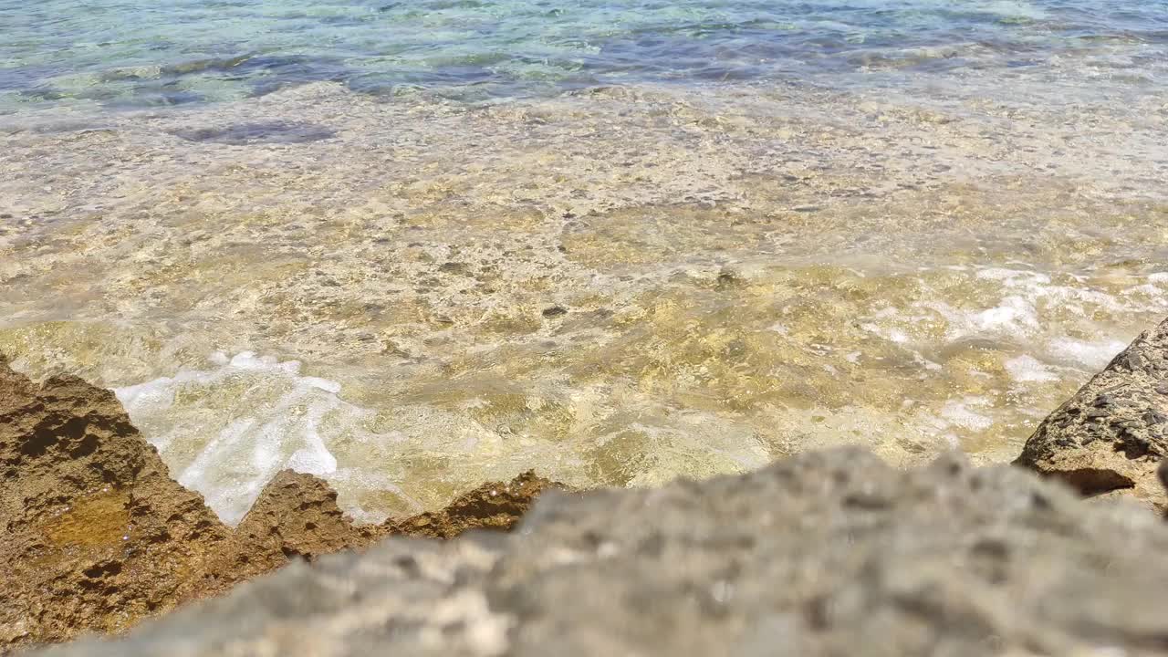 清澈的海水靠近岩石海岸的石头。在一个阳光明媚的夏日，一股小浪涌上海岸。一种放松、和平和宁静的气氛视频素材