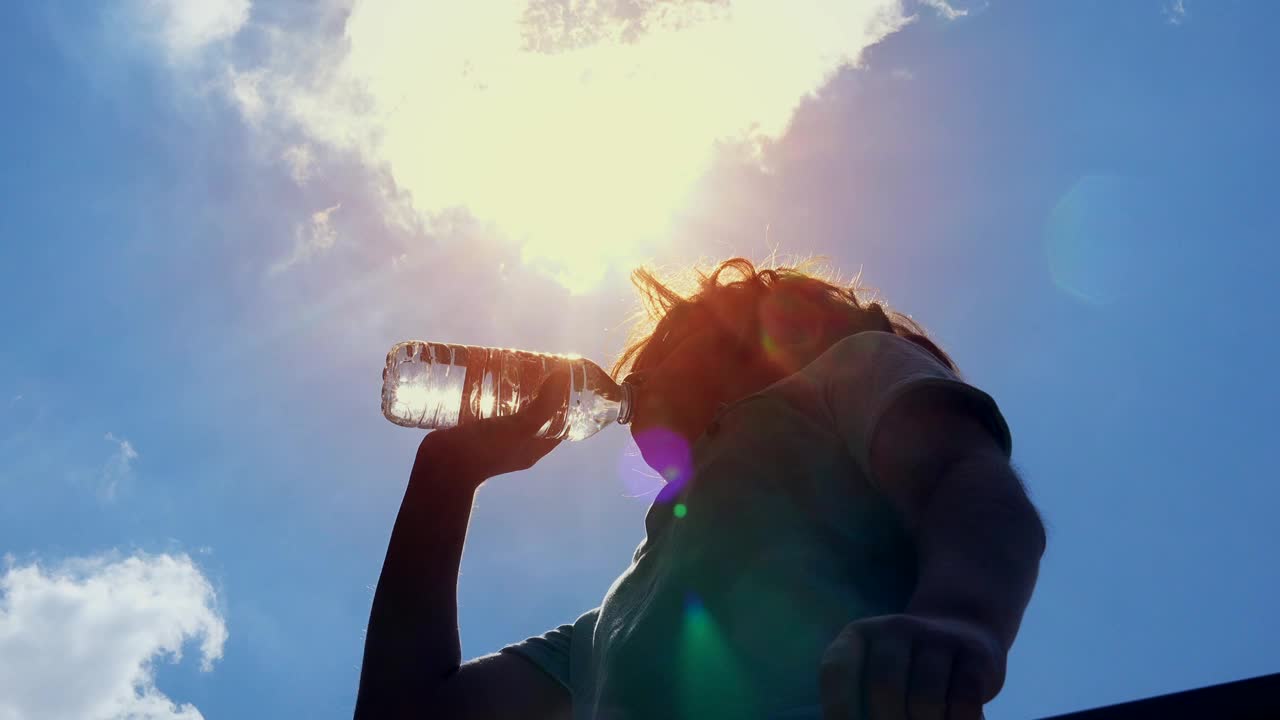 一个男孩在阳光明媚的大热天用瓶子喝水。视频下载