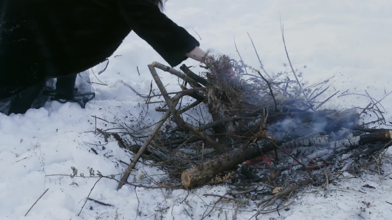 一名妇女在森林被雪覆盖的景观中，在篝火中添加干草视频素材