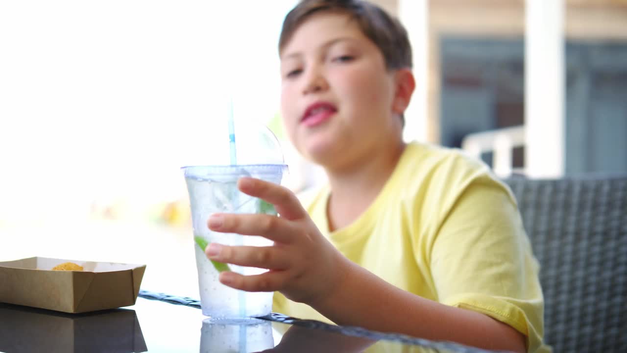 可爱的小男孩在海滩上喝着鸡尾酒莫希托吃着鸡块。视频素材