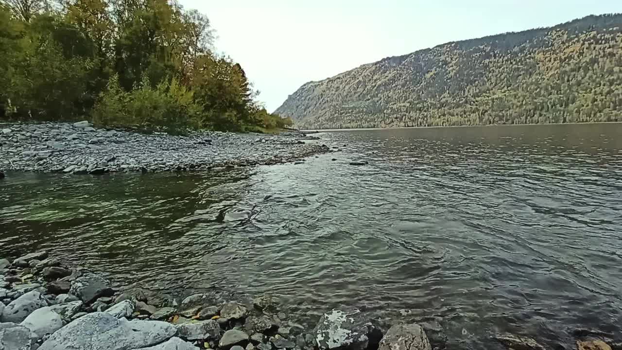 在多云的秋日里，山间小河汇入一个宽阔的湖泊处，岩石嶙峋，坡度平缓的海岸。视频素材