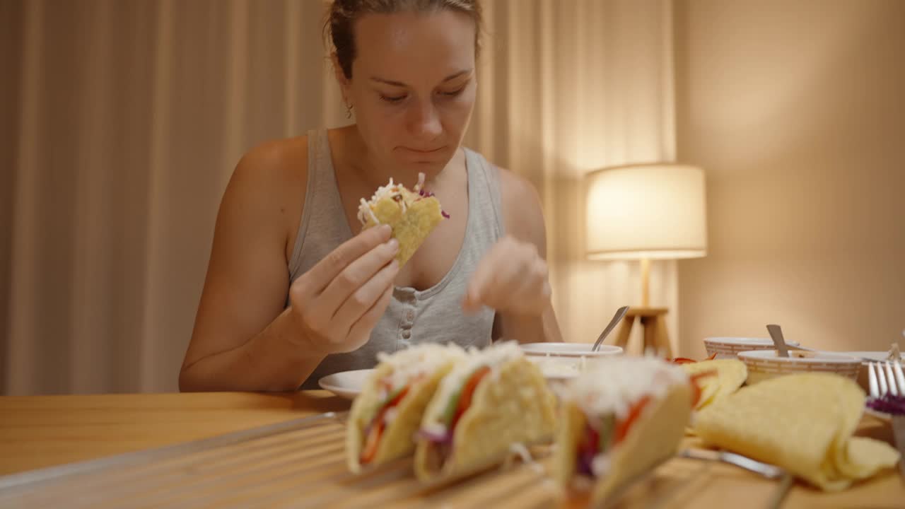 一个女人倾身吃了一口美味的墨西哥卷饼，里面装满了新鲜的食材，桌子上准备了更多的墨西哥卷饼。视频素材