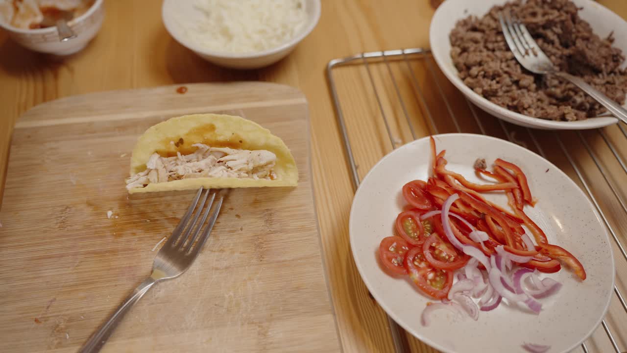 一只手把新鲜的鳄梨片放进装满鸡肉的墨西哥卷饼壳里，周围是切好的蔬菜和碎肉。视频素材