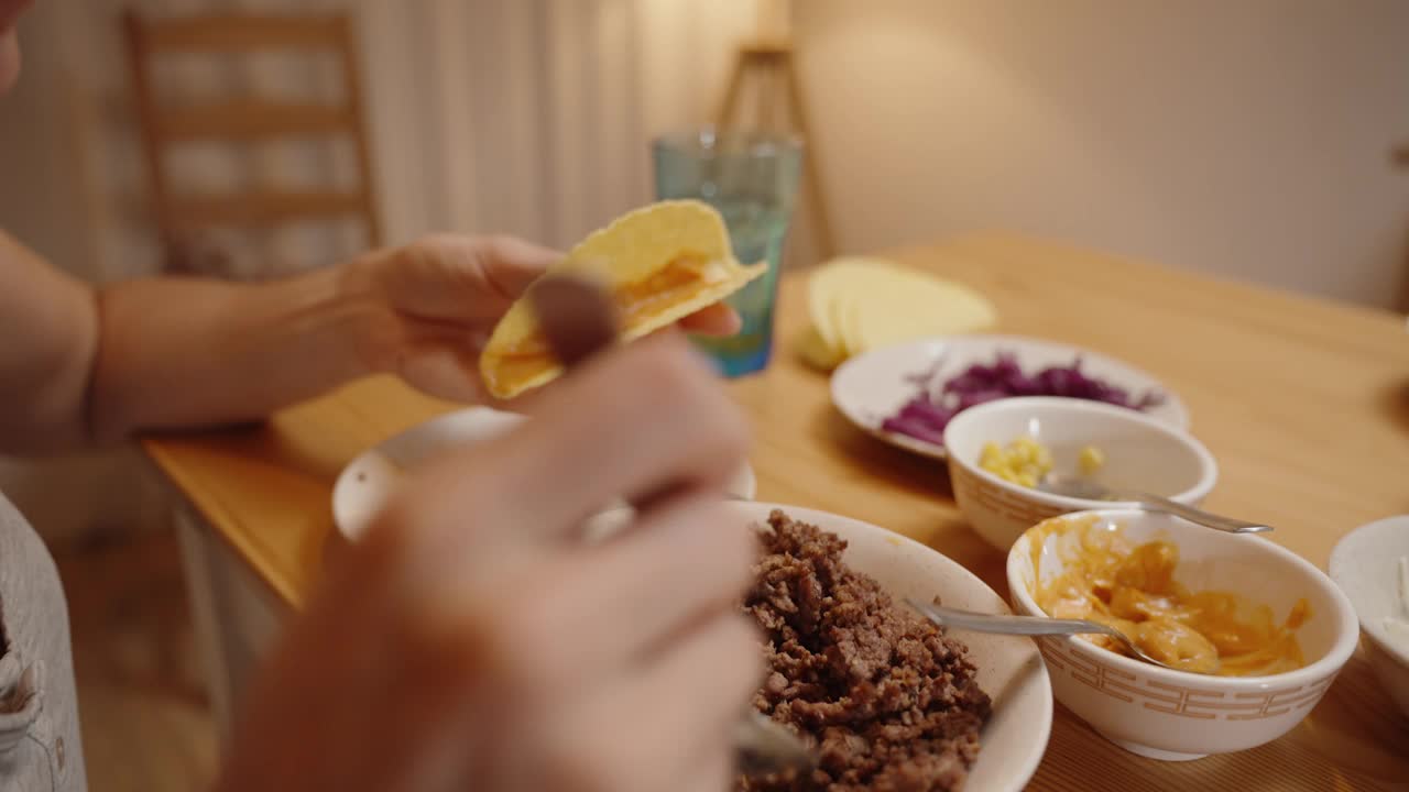 一个人用磨碎的肉填满玉米饼壳，用叉子加配料，在桌子上放上各种各样的配料。视频素材