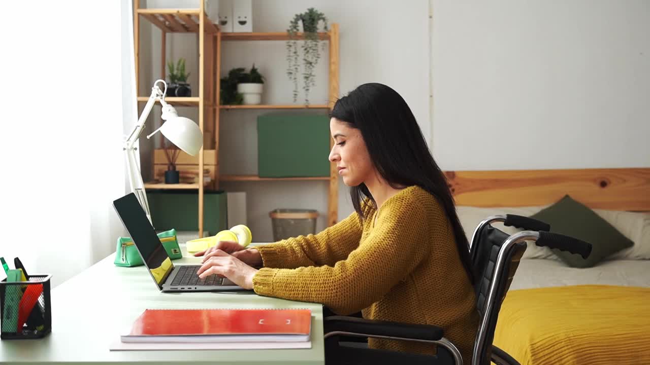 坐在轮椅上的残疾妇女在家办公桌旁用笔记本电脑工作视频素材