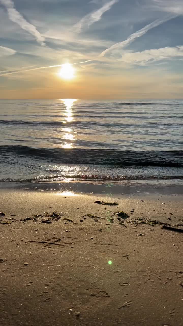 橙色的夕阳天空与云彩的背景下，海浪和海岸。鼓舞人心的平静的大海与日出的天空。水面上五颜六色的地平线。波浪的缓慢运动。垂直视频视频下载