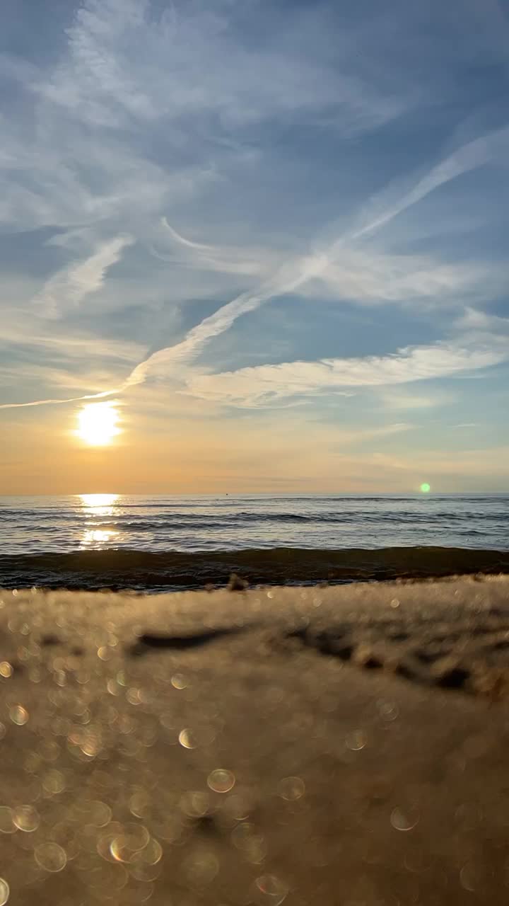 橙色的夕阳天空与云彩的背景下，海浪和海岸。鼓舞人心的平静的大海与日出的天空。水面上五颜六色的地平线。波浪的缓慢运动。垂直视频，延时播放视频下载