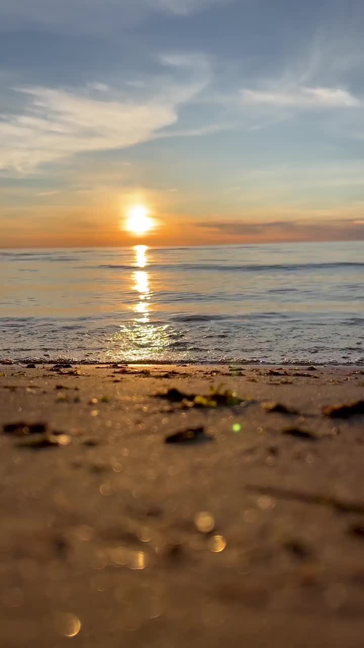 橙色的夕阳天空与云彩的背景下，海浪和海岸。鼓舞人心的平静的大海与日出的天空。水面上五颜六色的地平线。波浪的缓慢运动。垂直视频视频下载