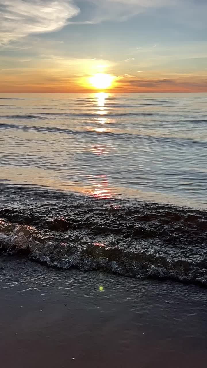 橙色的夕阳天空与云彩的背景下，海浪和海岸。鼓舞人心的平静的大海与日出的天空。水面上五颜六色的地平线。波浪的缓慢运动。垂直视频视频下载