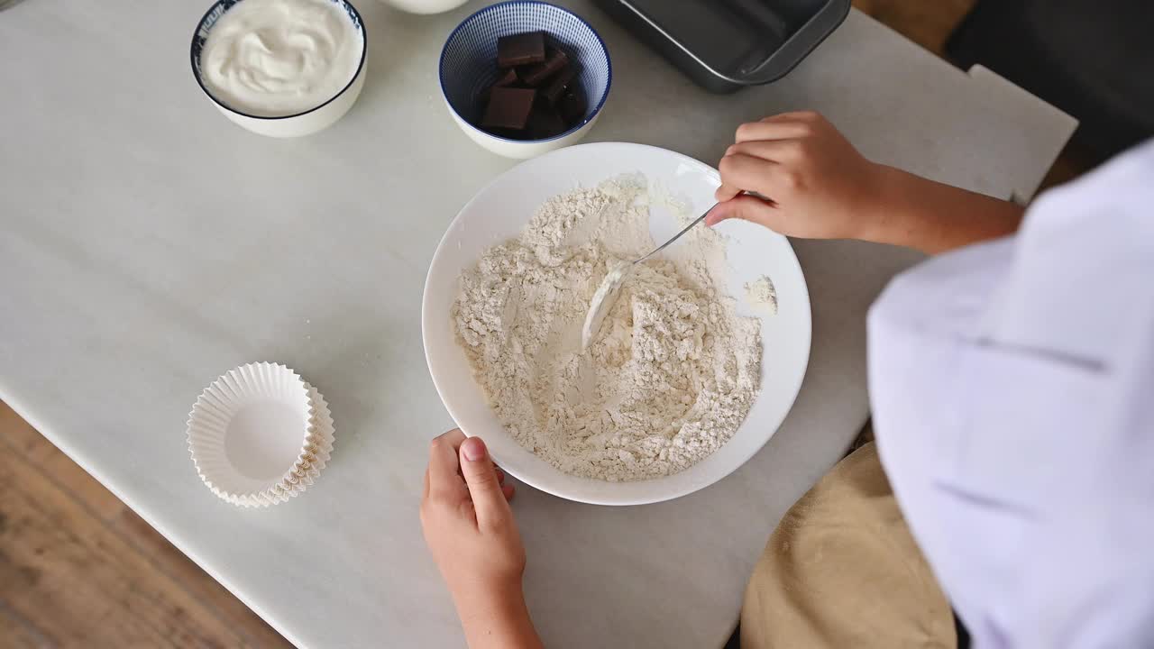 孩子在碗里混合面粉和桌上的烘焙原料视频素材