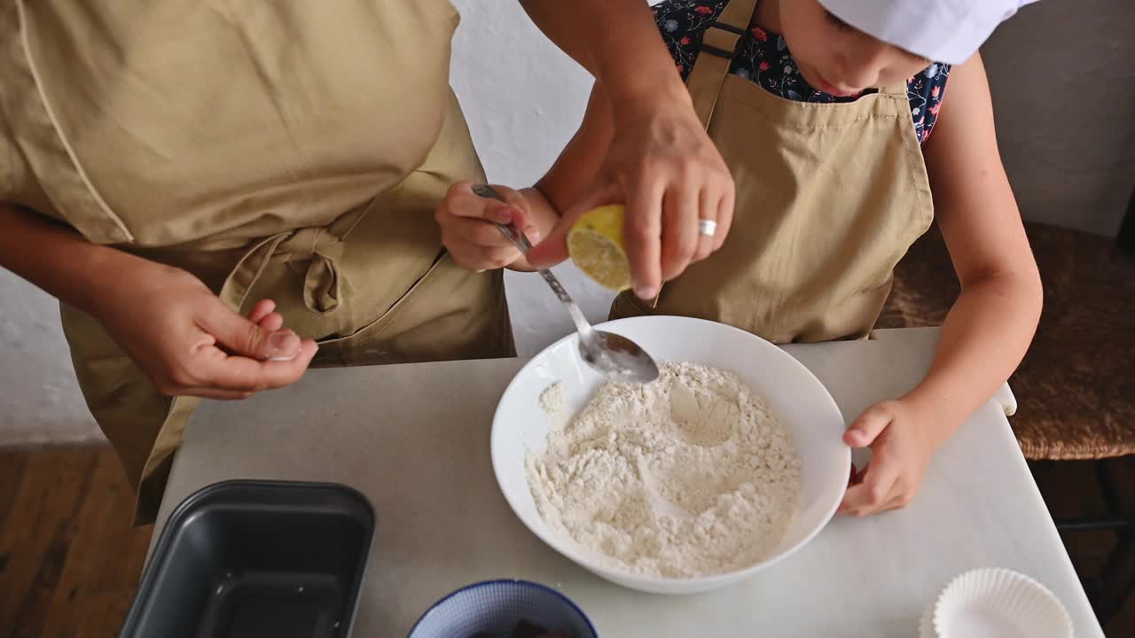 妈妈和孩子在厨房里一起烤，把配料加到一碗面粉里视频素材